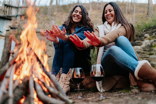 2 friends sitting round a campfire drinking wine